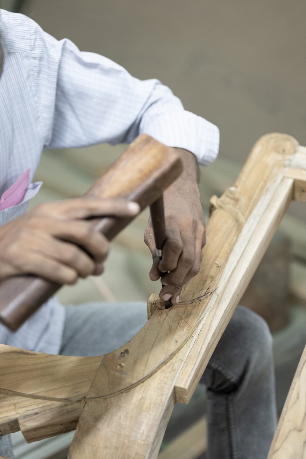Hands shaping a chair frame with a mallet and chisel